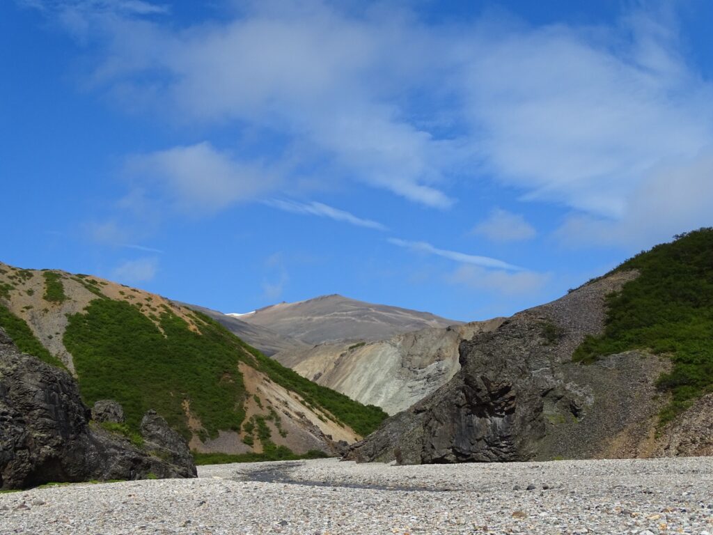 The view into Hvannagil or the golden valley. Blues skies hover over light coloured hills with some greenery. 