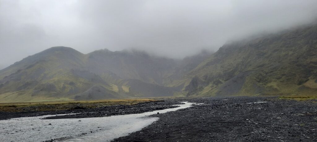 The first river crossing on the F249 towards Þórsmörk. The water is coming out of the mountains from the direction of the gorge Merkurker. The tops of the hills are covered in mist just like the rest hids behind a thin layer of fine rain. The water if the river flows over dark rocks.