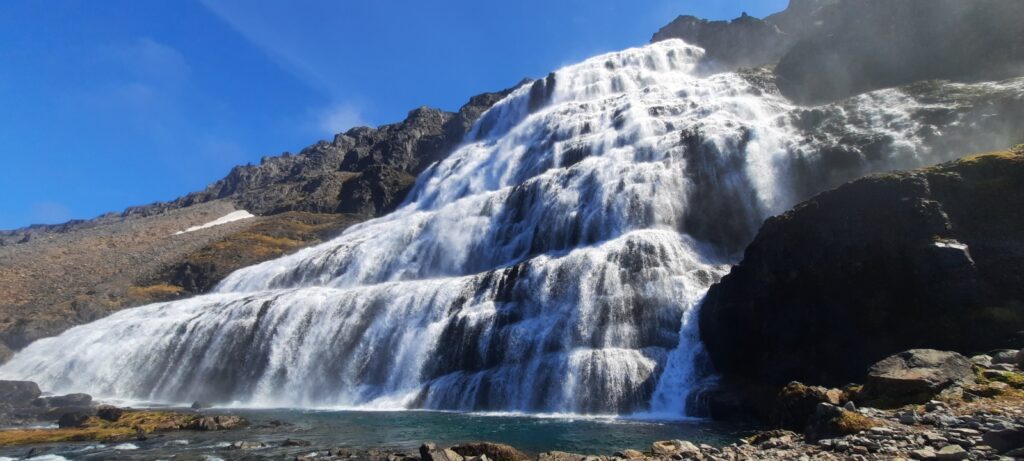 The waterfal Dynjandi looks like a bridal veil roaring of the mountain. With the clear blue sky and the sun shining the mist of the waterfall is very visible. 