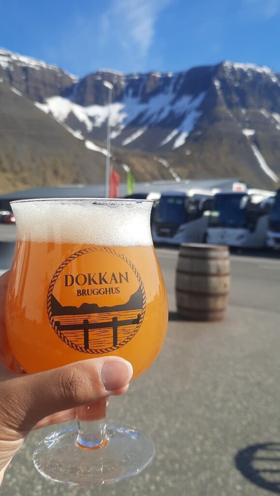 A hand holding an orange coloured Dokkan brugghús beer with the Trolls' seat (or Naustahvilft) in the back.